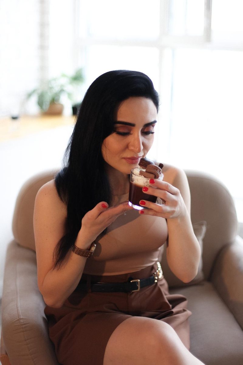 Nigar Rustamova in an armchair, smelling a chocolate dessert candle topped with whipped wax and macarons.