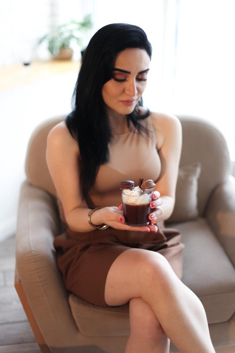 Nigar Rustamova in an armchair holding a chocolate dessert candle with whipped wax and macarons.