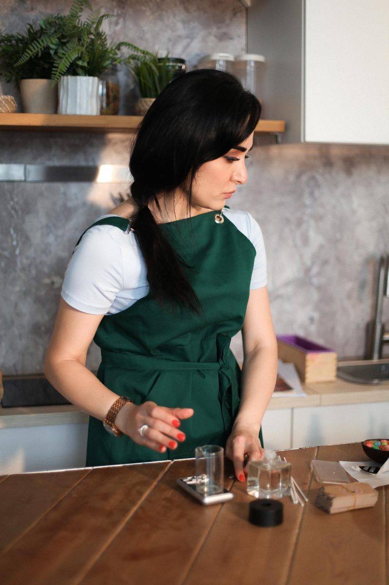Nigar Rustamova at her workbench with a scale, a measuring beaker and a glass reed diffuser bottle.